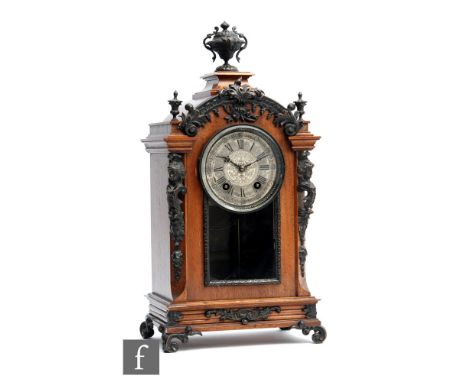 An early 20th Century walnut mantel or bracket clock of stepped arched form, with gilt metal urn shaped finial above caryatid