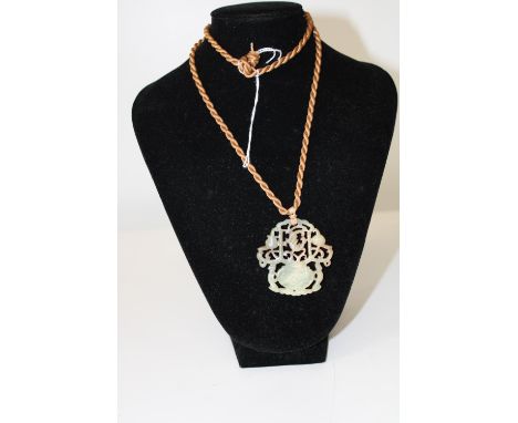 A carved jade pendant on gold silk braid 
