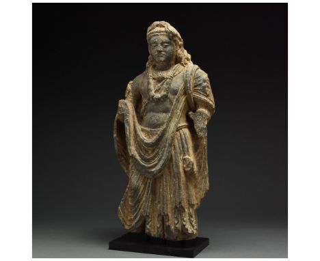 100 – 300 AD. Gandharan. A majestic schist standing buddha figure. The figure, bare-chested, wears an elaborate robe about hi