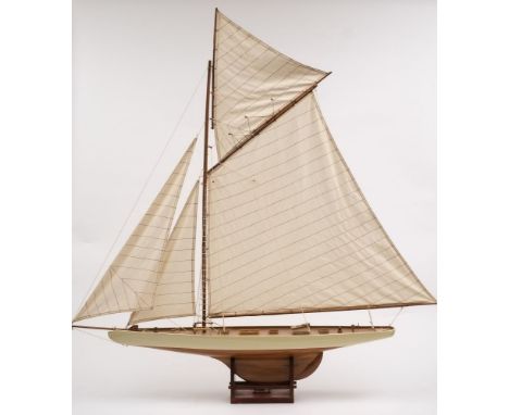 A model sailing yacht:, fully rigged and set sails over a planked deck with helm detailed fittings, the hull painted white to