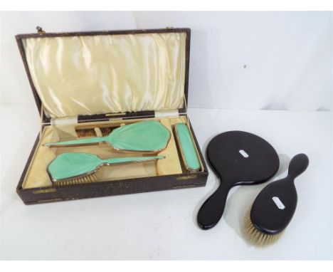 An enamelled dressing table set contained in original case comprising hand mirror, brushes, comb and an ebony hand mirror and