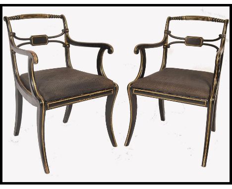 A pair of early 19th century Regency ebonised and gilt parcel armchairs. Raised on reeded sabre supports with drop in seats. 