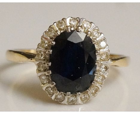 A ladies 18ct yellow gold sapphire and diamond ring, the oval cut central sapphire claw set surrounded by a band of small dia