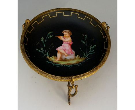 A mid 19th Century continental porcelain circular dish in engraved gilt metal scrolling stand, the centre painted with an inf