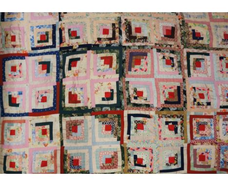 An early to mid 20th Century log cabin patchwork quilt made up of multiple coloured squares, each with central red patch surr
