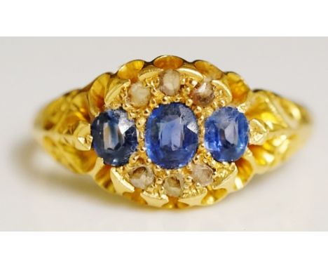 An 18ct yellow gold sapphire and diamond ring, the tablet set three oval cut pale sapphires surrounded by six small diamond c