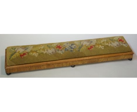 A Victorian walnut veneered long stool, the stuffed over top upholstered in floral gros point, sloping front on lobed black c