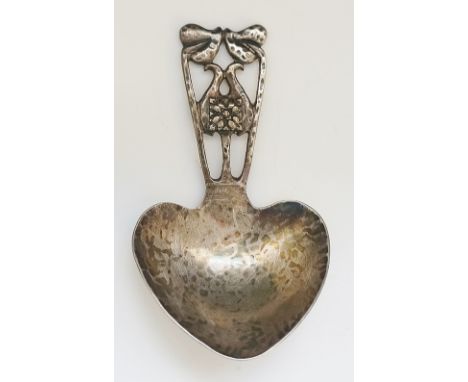 A silver Arts and Crafts caddy spoon, the handle in the from of stylised leaves and flowers, hammer textured heart shaped bow