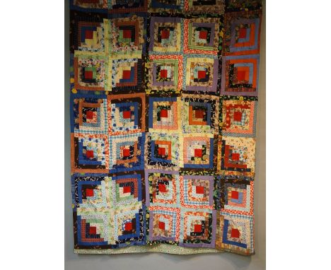 An early to mid 20th Century log cabin patchwork quilt made up of ten by ten multi coloured squares, each with central red pa