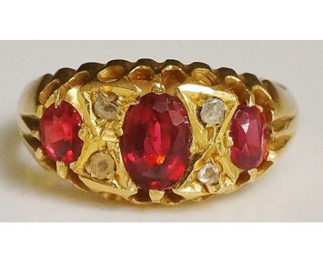 A ladies 18ct yellow gold ruby and diamond ring, the tablet pavé set with one large and two smaller oval cut rubies, flanked 