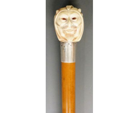 A 19th Century walking stick, the ivory terminal carved as Mephistopheles, faceted glass chip eyes, silver coloured metal col