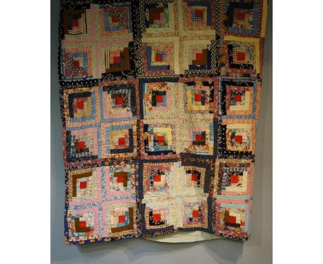 An early to mid 20th Century log cabin patchwork quilt made up of ten by ten multi coloured squares, each with central red pa