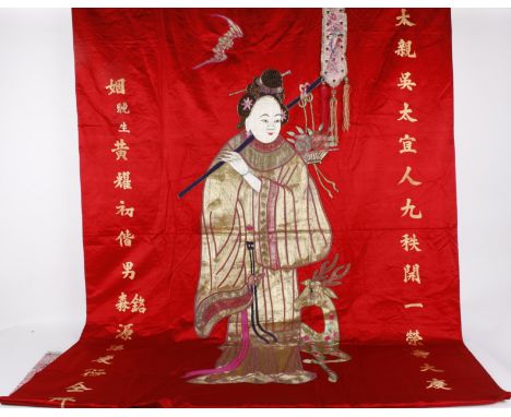 A Chinese red silk wall hanging with a central appliqué figure of a woman, her robe is finely worked in gold metallic thread,