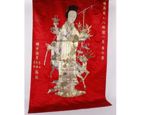 A Chinese red silk wall hanging, with a central female figure embroidered with gold and coloured threads couched in red with 