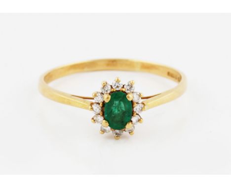 An 18ct yellow gold cluster ring, with central oval cut emerald, 5mm by 4mm, surrounded with a frame of diamonds, bears hallm