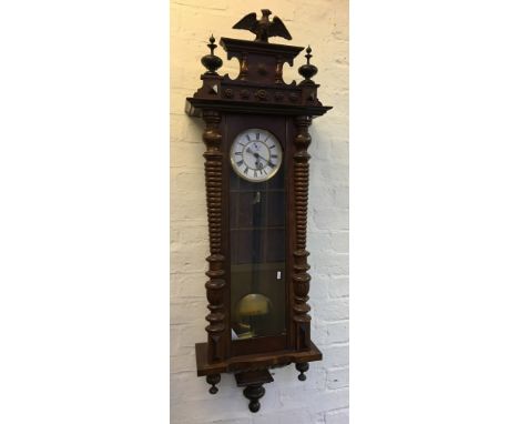 An early 20th Century wall hanging clock in mahogany clock with carved column supports, with pendulum and weight.