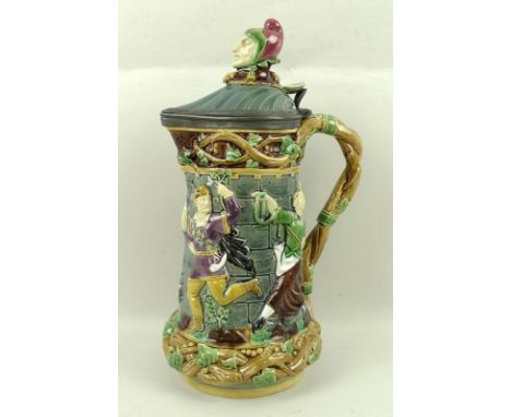 A Minton Majolica Jester tower jug, with moulded dancing figures, the shell shaped lid with jester finial, with pewter hinge 
