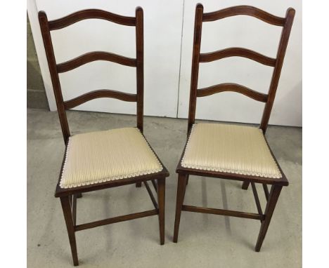 A pair of Edwardian ladder back chairs with inlaid banding and gold striped upholstery.