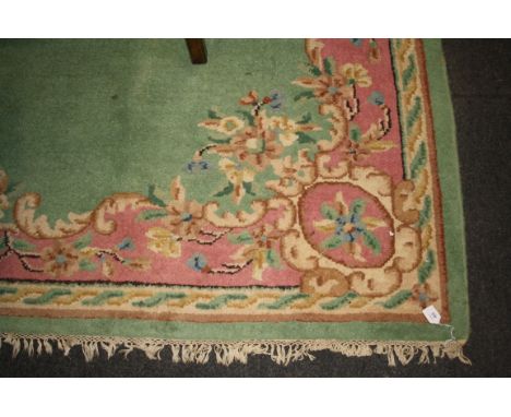 A 20th century Chinese wool carpet, woven with a central oval floral reserve within a conforming guard on an apple green and 