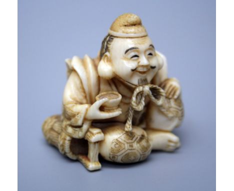 A 19th century Japanese carved ivory netsuke of a seated smiling man, with string tied hat and rice bowl, red seal signature 