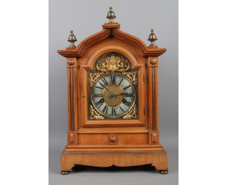 A substantial walnut mantle clock, with ornate brass dial featuring Roman Numeral markers and brass finials to the arched top