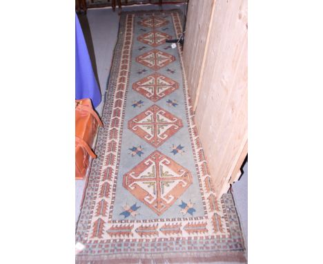 A Kazak design runner with six diamond lozenges in shades of fawn and natural on a light blue ground, 33" x 117" approx