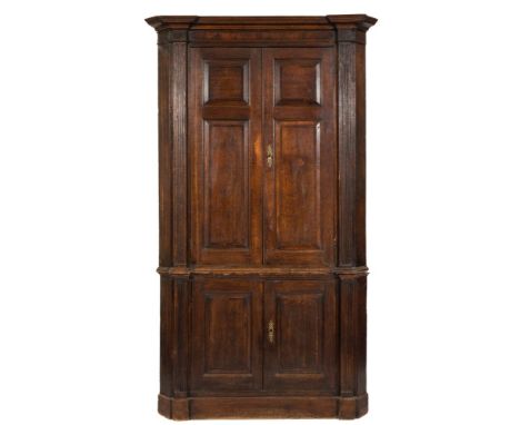 An 18th Century oak and mahogany Architectural standing corner cupboard:, in two parts, the upper part with a moulded cornice