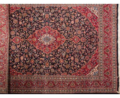 A Kashan carpet:, the indigo cartouche field with a central red cartouche pole medallion, all over scrolling palmette and flo