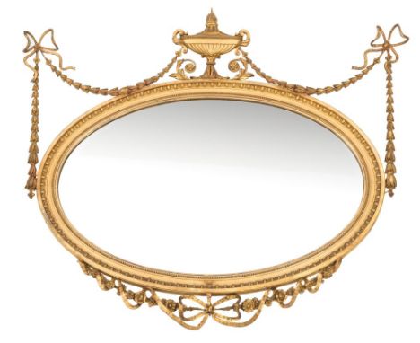 A carved giltwood and gesso oval mirror in the neo-classical taste:, surmounted by a central flaming urn and ribbon tied husk
