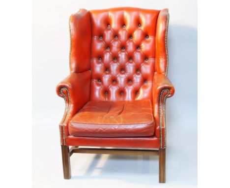 A reproduction Georgian style wingback armchair, in red leather with button upholstered back and loose seat cushion, on squar