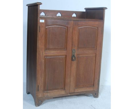 An early 20th Century oak arts and crafts Liberty of London cupboard having a gallery top with pierced heart decoration, the 