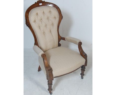 A 19th Century Victorian arm chair having a carved mahogany show wood frame with a spoon back, button back upholstery with pa