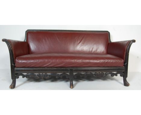 An early 20th century 1920's oak and red leather club / salon sofa having scrolled arms with an overstuffed seat with a folia