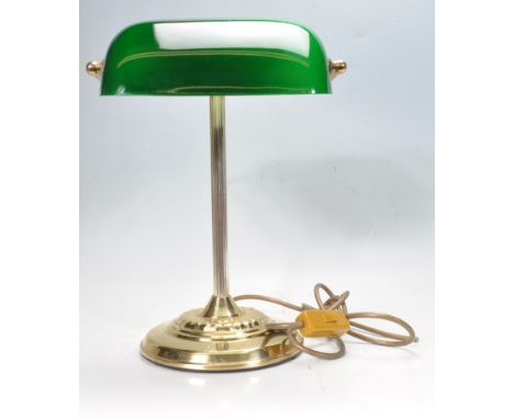A vintage 20th Century bankers desk lamp having an adjustable green glass shade raised on a brass support and repousse decora