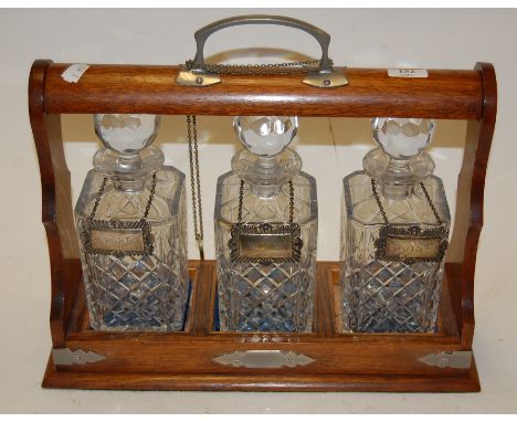 A 1920s oak three bottle tantalus with silver plated mounts, each decanter with silver plated label enclosed by a locking sti