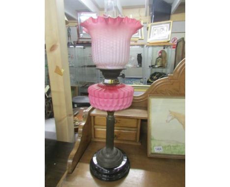 A brass oil lamp with pink glass font and shade (shade is cracked, there are blemishes to shade and font, dints to burner).