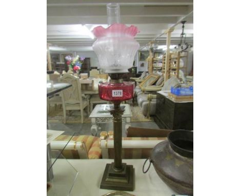 A brass Corinthian column oil lamp with cranberry font and later shade.