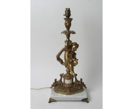 A gilt metal table lamp in the form of a cherub and raised on a squared white marble base.