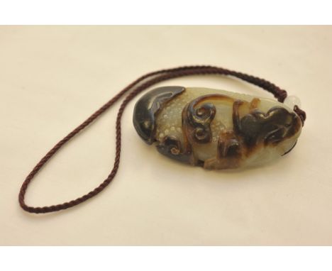 A carved jade two tone pendant in the form of a stylized animal