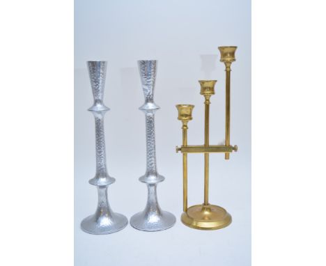 An adjustable triple sconce brass candlestick having narrow rod supports and shaped flared sconces and a pair of silver colou