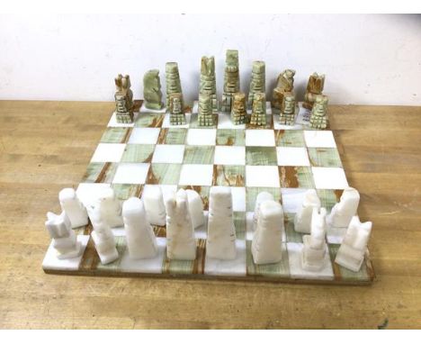 A polished and carved stone part chess set, lacking one pawn, board measures 36cm x 36cm