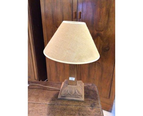 An oak table lamp with obelisk style stem on foliate carved base, having jute lined lampshade, measures 50cm high