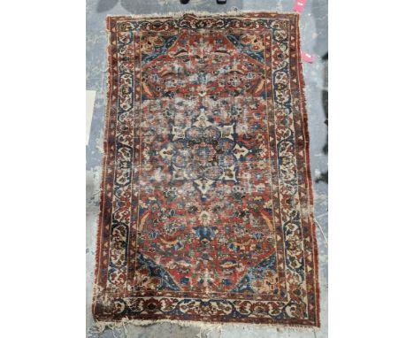 Eastern red ground rug with central floral medallion, stylised floral field, blue spandrals to geometric and herati borders, 