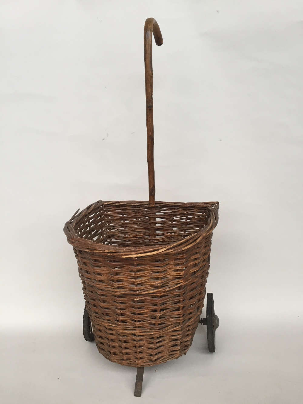 A vintage wicker shopping trolley with cane walking stick handle, three