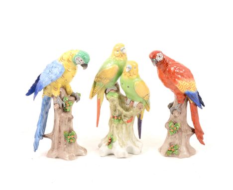 Pair of Sitzendorf porcelain parrots, modelled as macaws perched on naturalistic tree stumps, 23cm; and a group of two parake