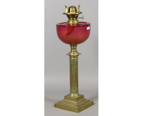 A Victorian oil lamp with reeded brass column base and cranberry glass font.