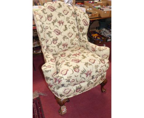 A walnut framed wing armchair in the 18th century style, the whole reupholstered in a floral decorated fabric, with squab cus