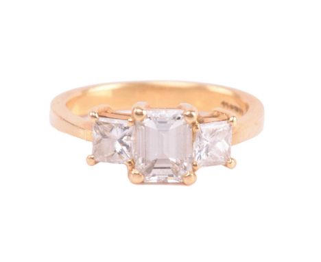 A diamond trilogy ring in 18ct yellow gold, scintillating with an emerald-cut diamond and two princess-cut diamonds on the si