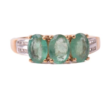 An emerald and diamond three stone ring, set with three oval emeralds in claw settings between double rows of round brilliant