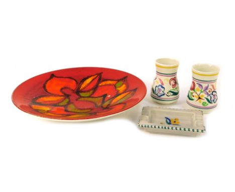 Four items of Poole pottery, comprising a Poole Delphis charger on an orange ground, 27cm wide, two circa 1960s Poole bud vas
